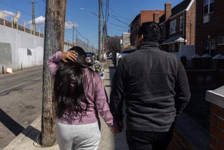 Two people hold hands and walk down a city street.