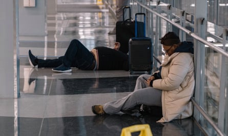 Two people with luggage lean on the glass partition of the moving walkway.