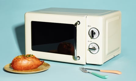 A plate with a baked potato on in front of a microwave