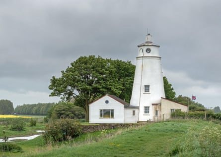 Small white lighthouse against rural background of trees etc.