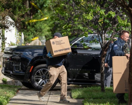 Homeland security officers carry boxes from the Washington residence of Ilhan Omar as yellow cordon tape can be seen in the distance.