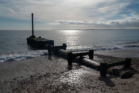 A wide sewage pipe running down a beach to a few metres off the beach