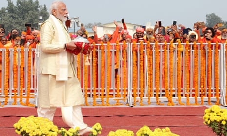 Narendra Modi walks, carrying an item on a cushion as people look on from behind barriers