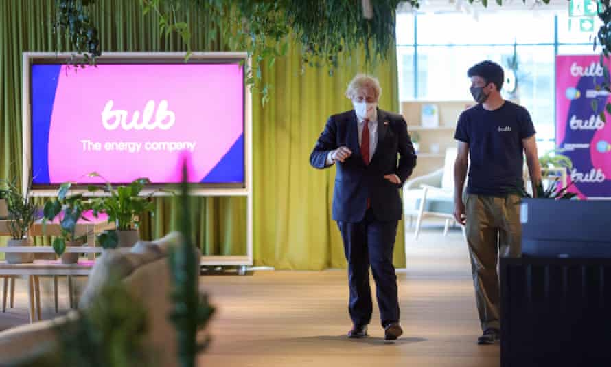 Boris Johnson ina. suit, and Haydsen Wood in a Bulb T-shirt, viewed from a distance walking through an open-plan office, with the Bulb energy logo visible on a large TV screen
