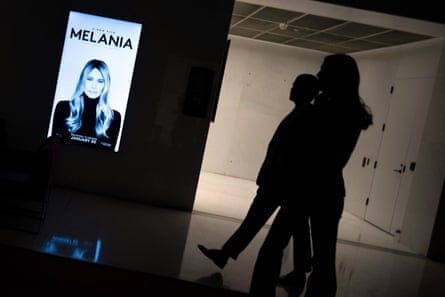 Two people walk past a Melania poster.