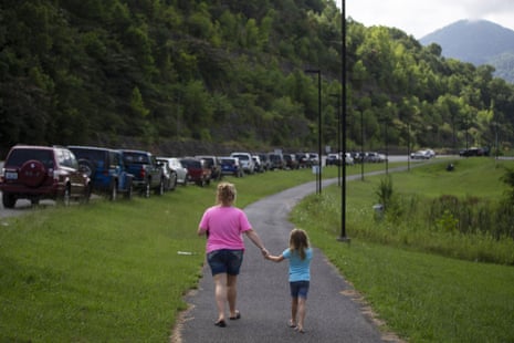 A mother and daughter walk past a line of miners’ cars down Highway 421 in Harlan, Kentucky. Many questions about Blackjewel’s operations have not been answered.