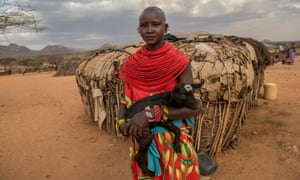 Portrait of a young Samburu woman holding a goat outside a hut.