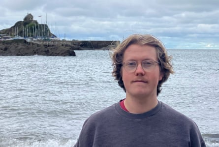 A young man standing against the sea and a rocky headland