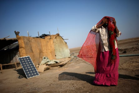 A labourer, who works in a salt pan, covers her face beside a solar panel outside a shelter