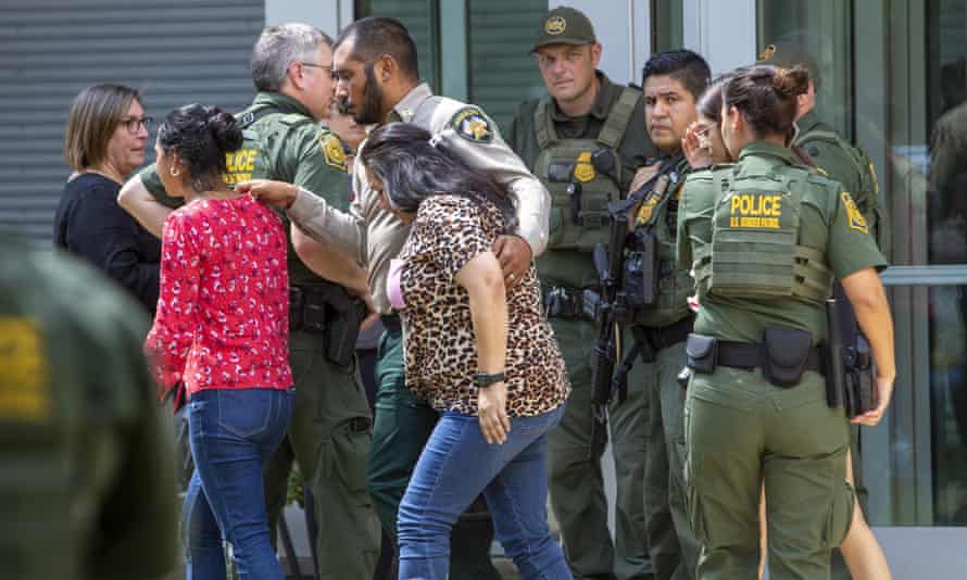 A group of officers escort families away from a building.