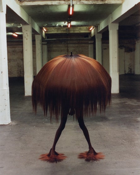A person wearing an umbrella covered in hair, which hides their head and body, and hair-covered shoes