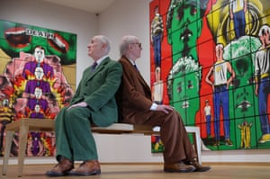 Gilbert & George pose on a bench in front of their artwork