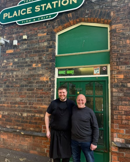 Two men smiling, standing outside a brick building with a sign reading Plaice Station