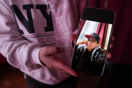 a woman holds a phone showing a photograph of a man wearing a baseball cap and smiling