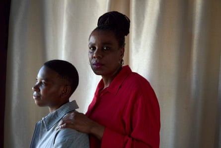 A middle-aged African woman looks at the camera while a teenager sits in front of her and looks away