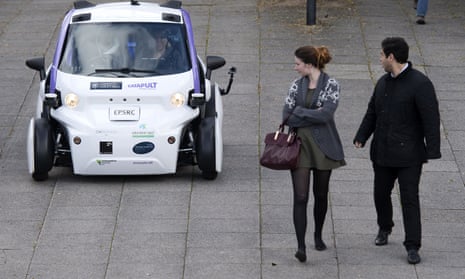Two pedestrians look round at a driverless car behind them