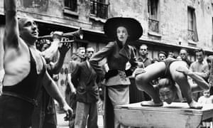 Elise Daniels with street performers in a suit by Balenciaga in Paris, 1948.