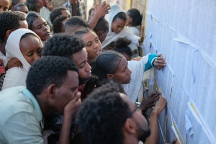 People crowd around a list of names pinned to a wall