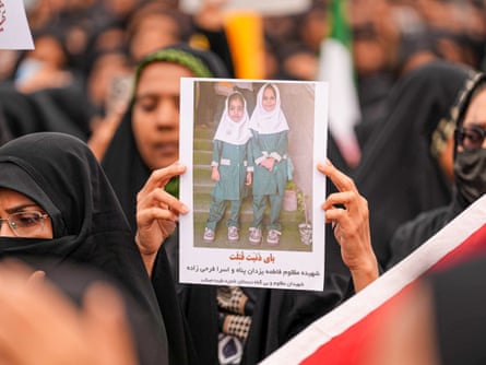 A woman holds up a photograph of two young girls in school uniform.