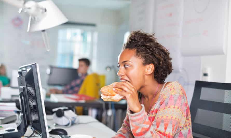 Businesswoman eating burger at desk.