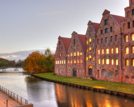 A row of old redbrick buildings on the banks of a river at dusk