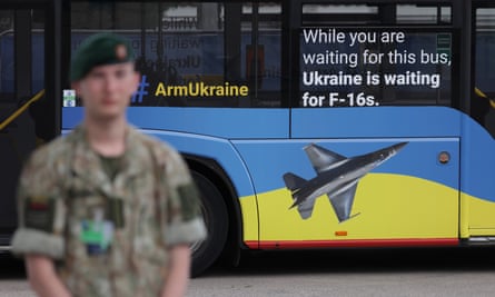 A Lithuanian soldier stands guard during the Nato summit as a public bus with livery promoting the arming of Ukraine passes by.