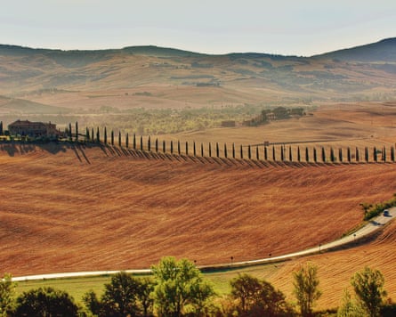 Automobiles drive through the beautiful Tuscan countryside on a bright sunny day.