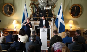 Humza Yousaf speaks from behind a lectern with two Scottish flags either side of him and a sign language interpreter to the left