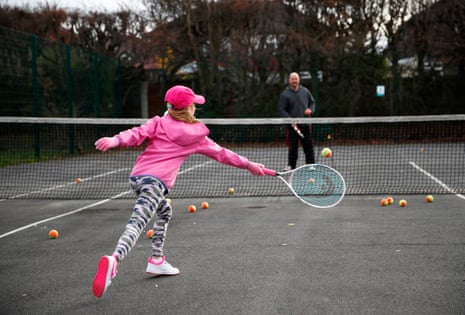 A young girl in a pink hat has one to one tennis coaching in a local park in Manchester