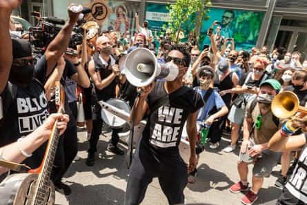 person wearing black shirt and sunglasses speaks into speakerphone in the middle of crowd
