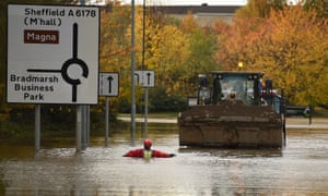 A member of the fire and rescue service wades through flood water as he escorts a JCB towing an truck along a flooded road Rotherham