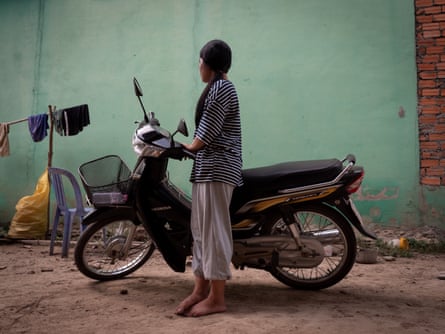 A women with face turned away standing next to a motorbike.