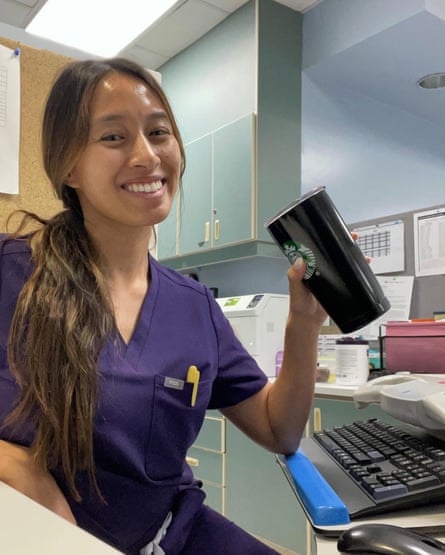 Woman in purple scrubs smiling at a desk, holding a Starbucks coffee.