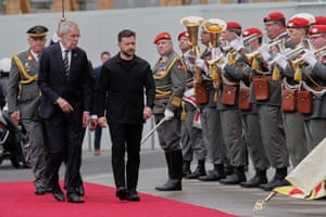 Two men walk on a red carpet past an honour guard and military band