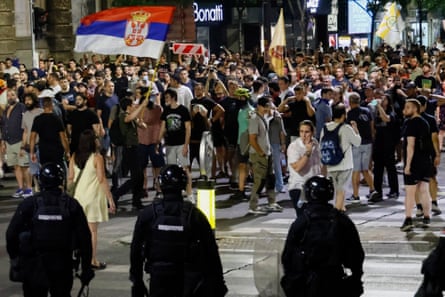 Riot police face off against a large crowd of mostly young people in the street, who are standing close together, some waving flags