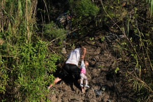 A Venezuelan migrant holds a child up as he climbs a river bank onto US territory, after crossing the Rio Grande river from Matamoros in Mexico