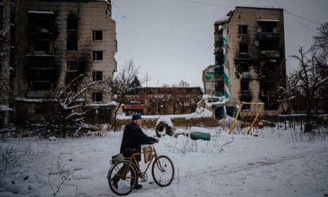 A man pushes a bike on a snow covered street next to destroyed residential buildings in Borodyanka, near Kyiv on 4 December.
