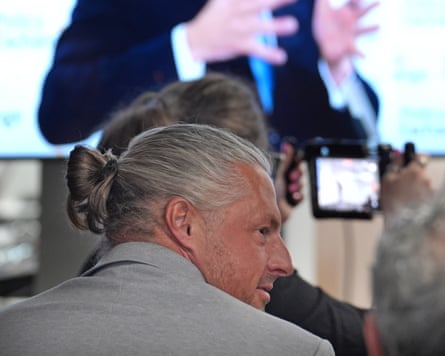 Ryan Bridge with his hair in a top knot, wearing a grey suit