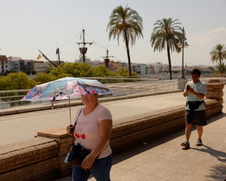 A woman holds an umbrella as she walks along a footpath in the sun