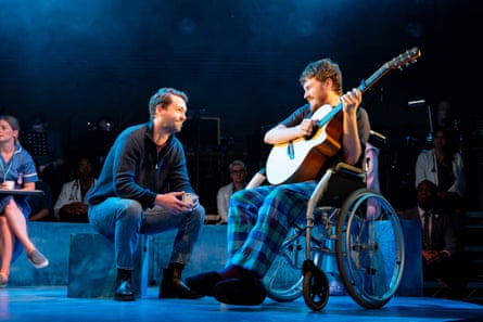 A man in a wheelchair with a guitar facing another seated man.
