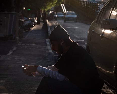 A man sitting on a kerb next to a parked car looking at his phone