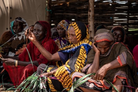 A group of women under a shelter, two of whom are working with leaves