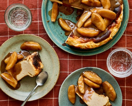 Two servings of toffee apple Basque cheesecake on small plates with spoons, alongside a larger plate with the rest of the cheesecake, all on a reddish chequered tablecloth.
