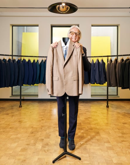 Paul Smith stands behind a jacket hung up on a rail inside a smart clothing shop, a long rack of jackets in the background.