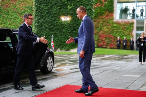 Andy Burnham and Friedrich Merz reach out to shake hands.