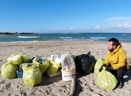 Suma kneeling on the beach next to a number of plastic bags filled with plastic items.