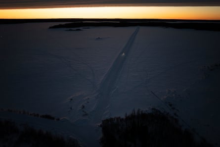 A truck traverses a frozen lake in the dark with the sun over the horizon