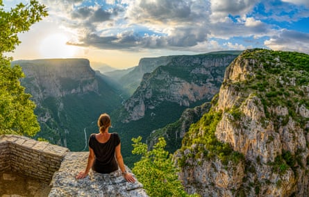 Rear view of a woman wearing a black T-Shirt sitting on a rock and looking deep down to the Vikos canyon in Greece