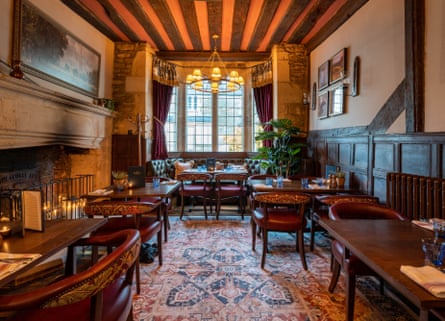 Interior of oldest pub of England with heavy wooden beams on ceiling and walls and tables set around a grand fireplace.