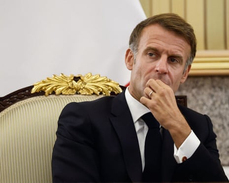 Emmanuel Macron sitting in a chair with his hand covering his mouth